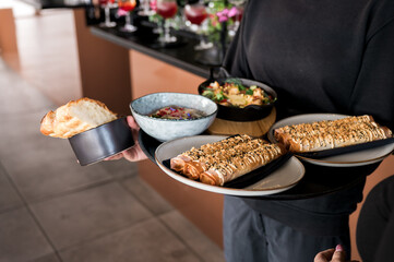 Elegant restaurant server carrying an assortment of gourmet appetizers, artisan bread, and beautifully plated dishes, showcasing upscale dining presentation and modern culinary style.