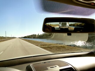 A road river seen through the rearview mirror windshield with a truck chasing.