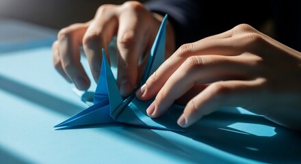 Hands folding blue paper origami crane on a light blue surface.