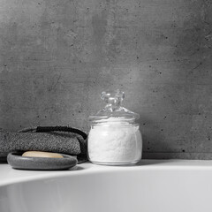Glass jar with natural sea salt in grey bathroom, stone soap dish with soap, exfoliating body washcloth. Modern eco-friendly approach to self-care and wellness routines, home spa routine