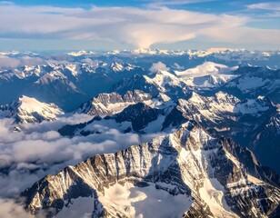 Aerial view of snow-capped mountain peaks partially obscured by clouds under a blue sky