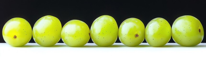 Seven glossy green grapes lined up in a single row on a white surface against a black background, fresh calm minimalist still life