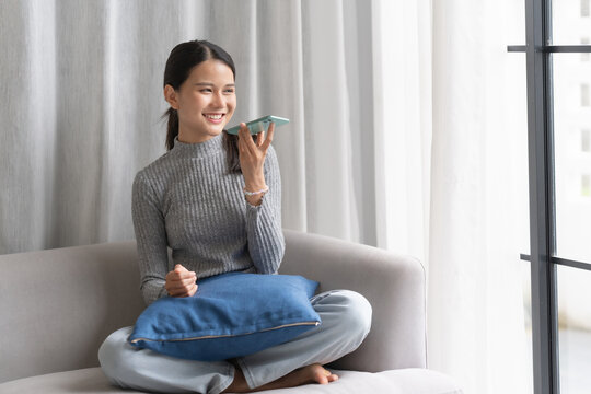 Asian woman using voice assistant on smartphone at home conversation with online assistant Voice chat bot conversational AI Modern Technologies.