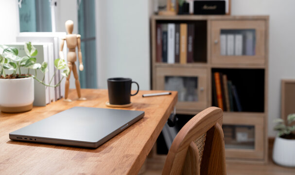 Closed laptop on a rustic wooden desk in a stylish home office, featuring a coffee mug and bookshelf in the background.
