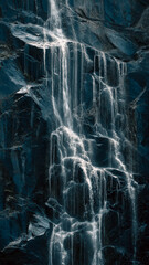 Dramatic Waterfall Cascading Down Dark Steep Textured Rock Face In Streaks Of Foamy Water.