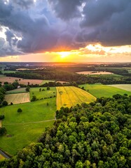 Aerial shot capturing fields and woods meeting in soft sunset light under dramatic skies