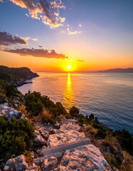A sunset over a rocky cliff, with a calm sea reflecting sunlight and a colorful sky, shot from above
