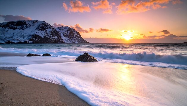 A sunset view of waves washing onto a sandy beach with snow-covered mountains in the background