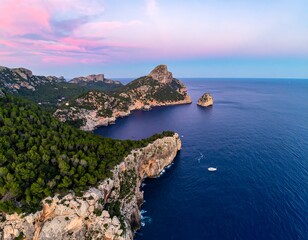 Aerial view of a rocky coastline with lush green trees and pink and blue sky over the dark blue sea