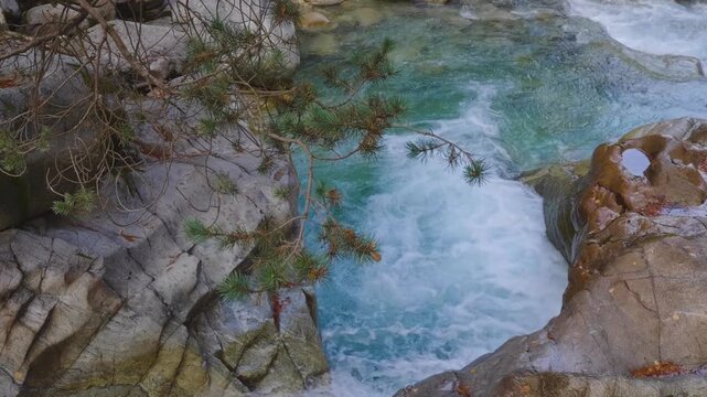 A shot of a clear, fast flowing mountain river cascading over rocks in a scenic gorge. The turquoise water rushes over smooth stones, surrounded by rugged, natural rock formations and lush green folia