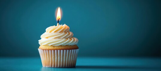 single vanilla cupcake topped with swirled buttercream and a lit candle on a teal background, warm celebratory mood