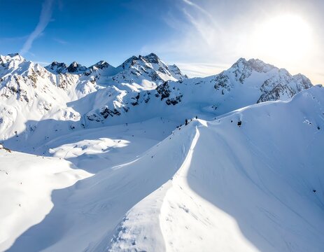 Aerial view of a snow-covered mountain range under a bright, clear blue sky with the sun shining