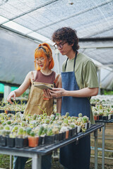 Young Asian Man and Woman Gardeners Working Together in Greenhouse with Tablet, Caring for Cactus Flowers and Plants