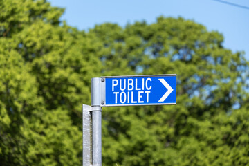 A blue PUBLIC TOILET directional sign mounted on a metal pole in Australia. Concept of community amenities, urban signage, toilet location guidance