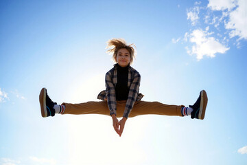 Teen girl performing a midair split jump against a bright blue sky with clouds. Generative AI