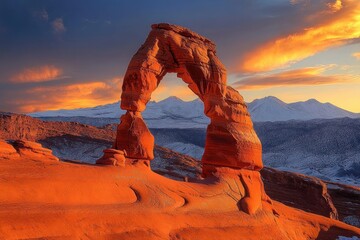 solitary red sandstone arch framed by snow-capped mountains and fiery sunset clouds, dramatic golden light evoking awe and tranquility