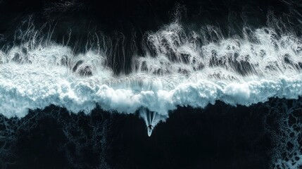 Aerial top-down view of a lone surfer on a surfboard cutting through a massive crashing white wave in a dark ocean, evoking isolation and exhilaration