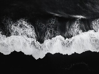 aerial view of dramatic black and white ocean waves breaking into foamy surf along a dark shoreline, powerful and moody