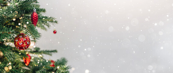 Christmas tree with red decorations on light background with bokeh, sparking, glowing. Merry Christmas and Happy New Year greeting card. Xmas and Winter holidays. Christmas wide banner