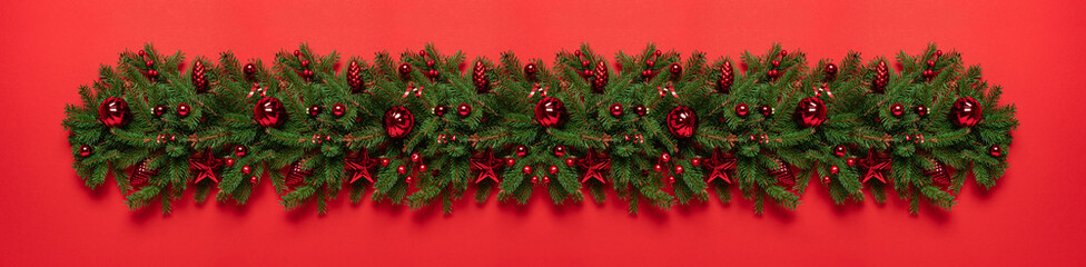 Christmas tree garland with red glitter decorations on red background. Merry Christmas and Happy New Year greeting card. Xmas and Winter holidays. Christmas wide banner, top view