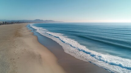 aerial view of a long empty sandy beach with gentle waves, a lone walker on the shoreline, distant mountains and a clear blue sky conveying calm and serenity