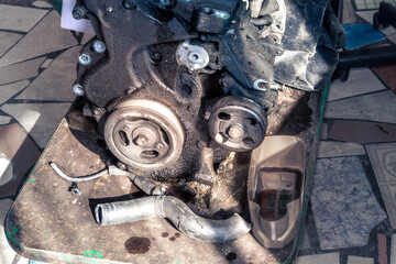 Old car engine sitting on a dirty cart with loose parts around it