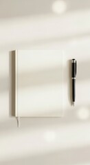 Plain ivory notebook and dark writing instrument rest on a light surface with subtle illumination patterns
