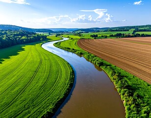 Aerial view of a winding river flowing through lush green meadows and cultivated fields under a bright blue sky