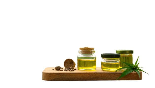 Golden liquid in jars with hemp leaf on wooden board, against black background