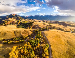 Aerial view of golden fields and hills meeting distant mountains under a partly cloudy, bright blue sky