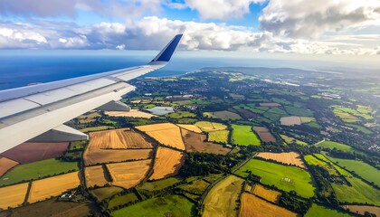Aerial view of patchwork fields and coastline seen from plane window under sunny, partly cloudy sky