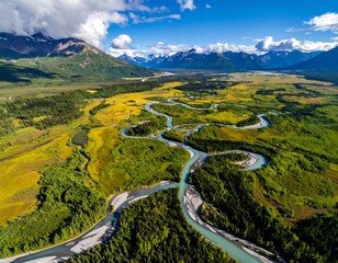 Aerial view of river winding through lush green valley, mountain range backdrop under a sunny blue sky