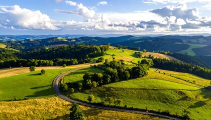 Aerial view of rolling hills, green fields, a winding road, and a dynamic sky with puffy clouds