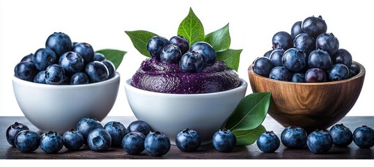 Two bowls of fresh blueberries and one bowl of blueberry puree topped with berries and green leaves on a wooden surface, vibrant and appetizing