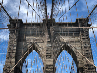 Fototapeta premium An abstract close-up view of a tower and the cables on the Brooklyn Bridge, looking up towards the American flag on a blue sky day