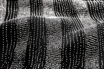 close-up of black fabric with undulating white dotted vertical stripes and textured draped folds conveying a calm, rhythmic abstract pattern