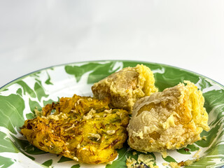 Indonesian fried snacks featuring bakwan and stuffed tofu on a green-white enamel plate. Traditional oily unhealthy street food. closeup. copy space