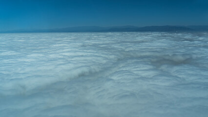 The solid surface of the clouds is visible from the airplane window. Mountains on the horizon. The blue sky. Peru