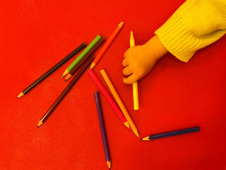 Childs Hand Reaching for Yellow Pencil Amidst Scattered Art Supplies