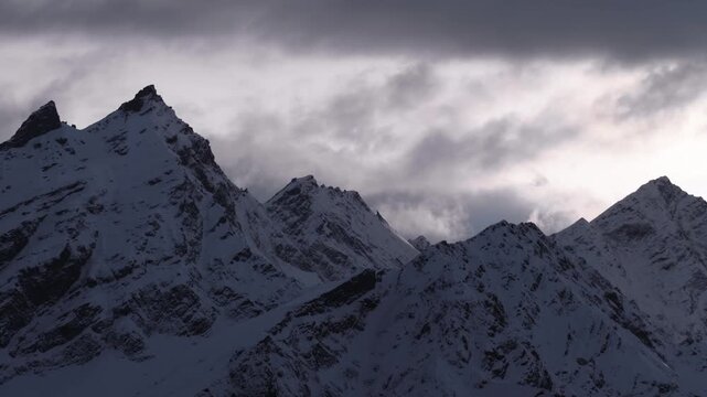 A wide shot of the rugged, snow covered peaks of the North Caucasus mountains under a dynamic, cloudy sky. This footage captures the vast and dramatic landscape of the region, perfect for projects rel