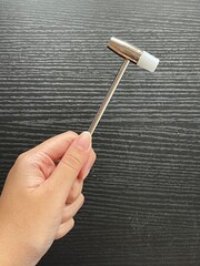 Close-up of a hand holding a small dual-head nylon hammer with a metal handle against a black wood background, showing a compact tool used for crafts and light repairs.