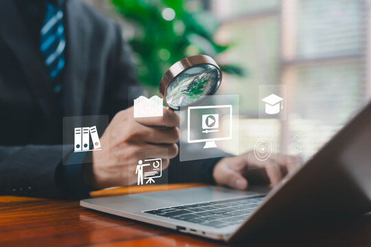 A business professional using a magnifying glass to review digital icons on a laptop, symbolizing data analysis, online learning, research, document management, and strategic evaluation in a modern