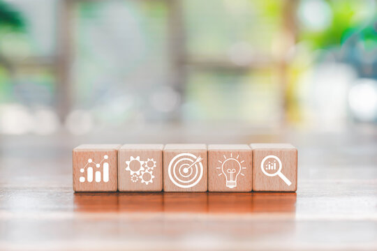 Wooden blocks with white business icons representing analytics, process, target, creativity, and data research on a blurred natural background, symbolizing strategy innovation, workflow improvement,