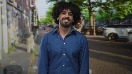 Man with open hands and outstretched palms on city street wearing blue shirt and watch facing camera; welcoming invitation.