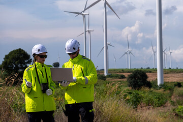 Engineers monitor wind farm performance with laptop in green jackets during daytime