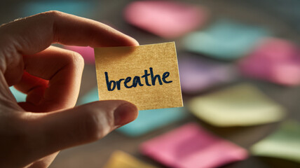 A hand holding a note with the word breathe on it, with other colorful notes in the blurred background. It evokes a sense of calm and mindfulness