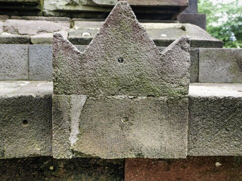 Close-up of an old stone architectural detail, possibly an antefix or stylized crown, covered in moss. Ancient ruins, weathered texture, and historical architecture.