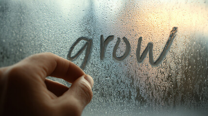 The word grow is being written on a foggy window with a hand. It's a reminder of new beginnings and personal development