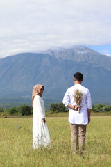 Fototapeta premium A Muslim couple in white outfits captured in a bright and serene prewedding moment, set against a stunning mountain backdrop under clear blue skies—elegant, pure, and full of love.