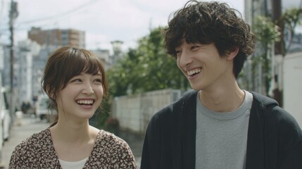 Two young adults share laughter while walking down a street lined with trees and buildings. They look joyful, enjoying their time in a vibrant city.